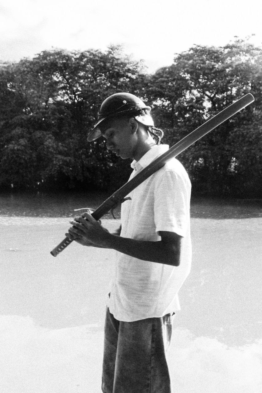 Fotografia em preto e branco de Rakim à beira de um rio, usando um capacete e carregando uma katana sobre o ombro